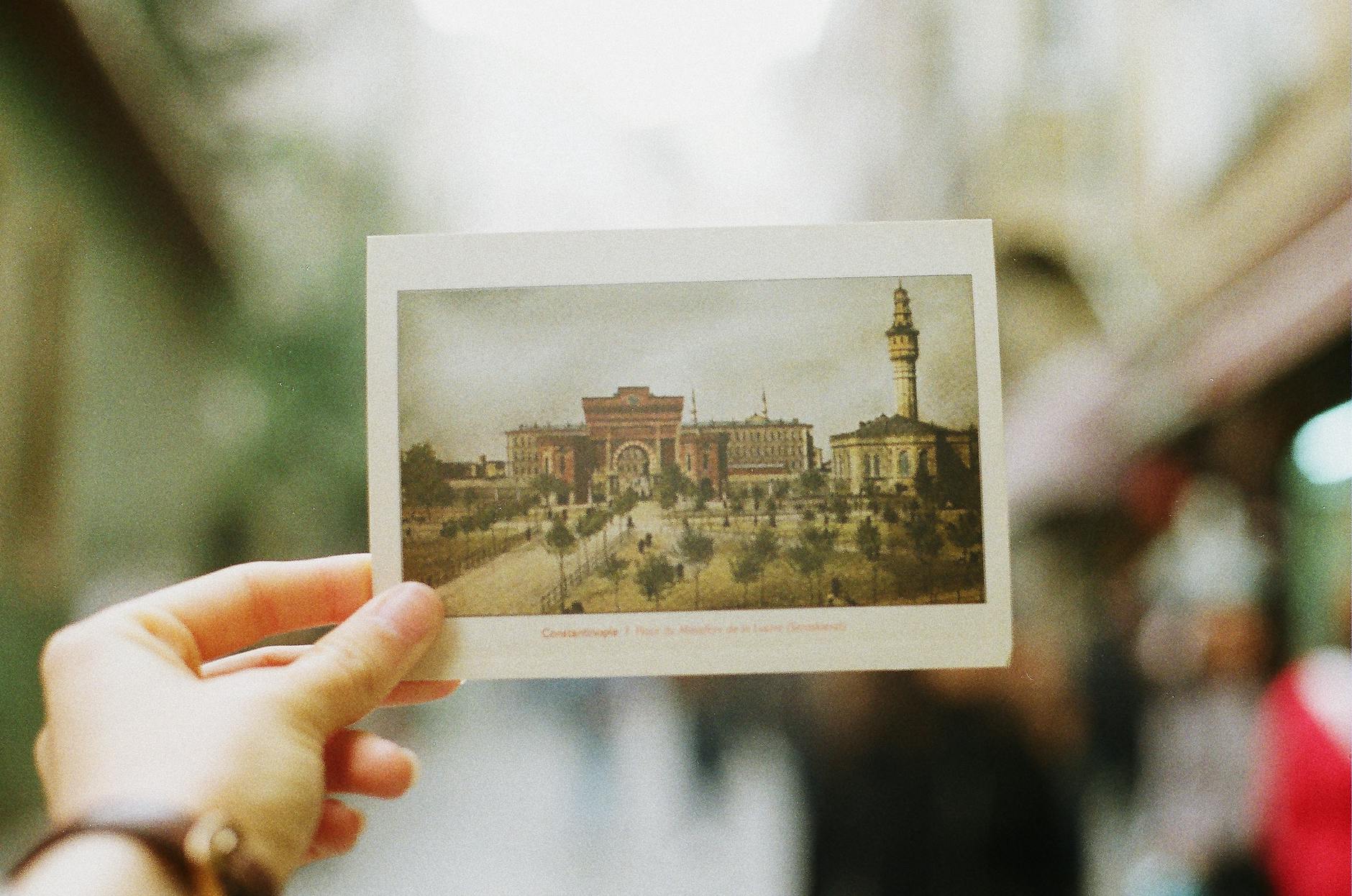 crop person showing postcard with photography of old city